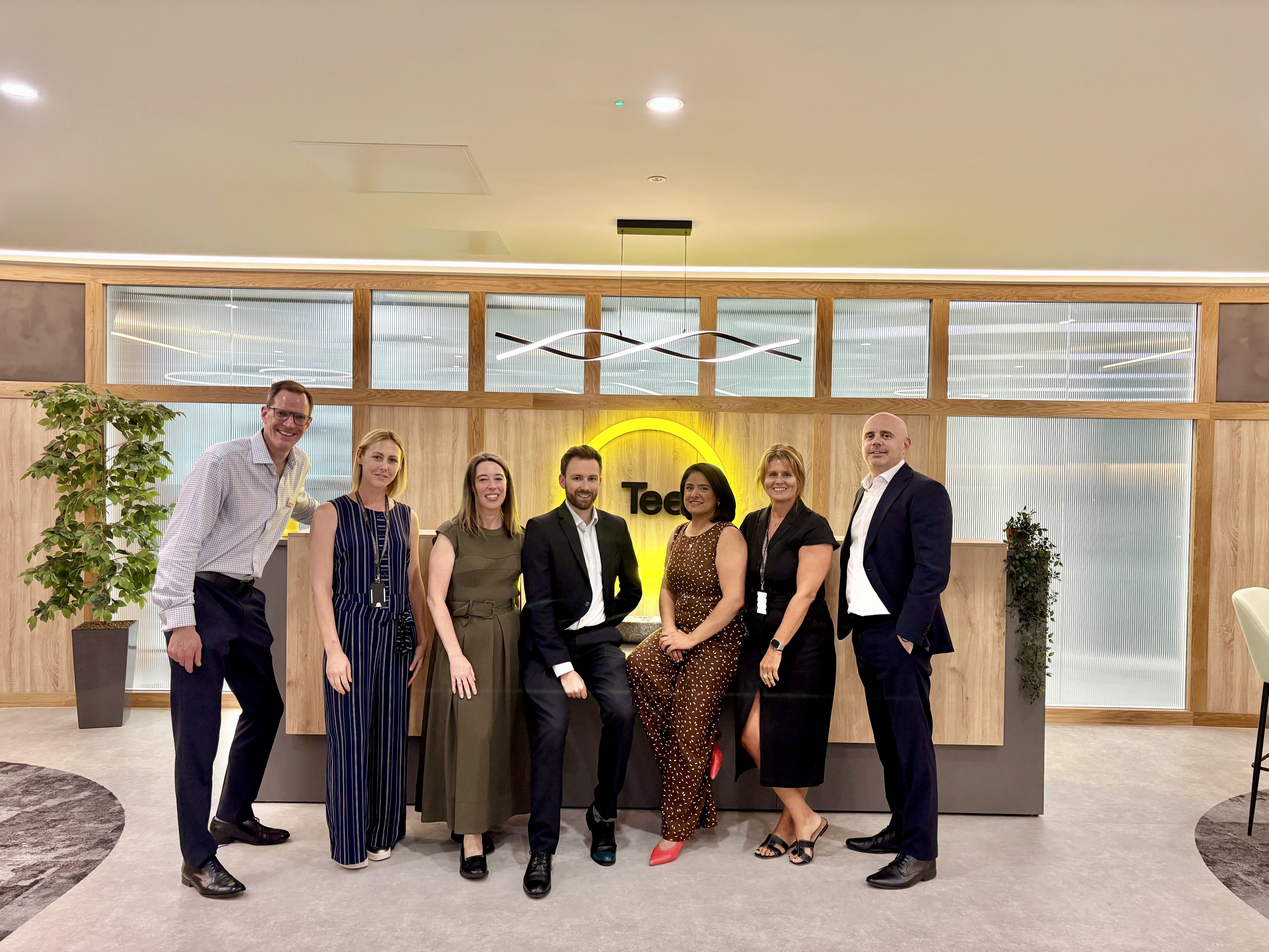 group of people stood in front of tees law logo in new office