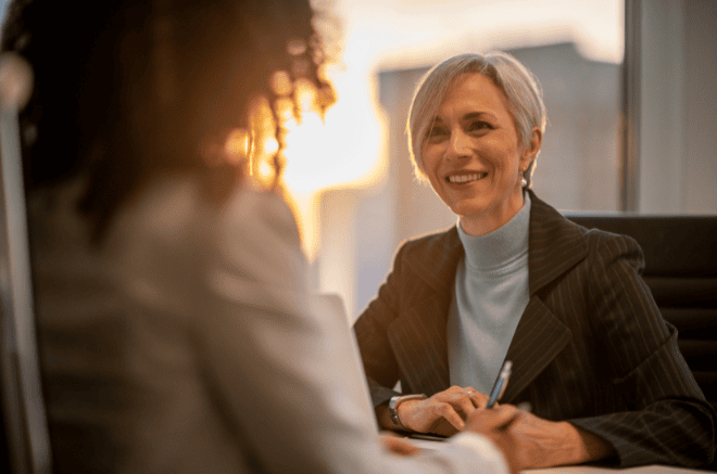 woman in a suit smiling over the table at another woman, costal property